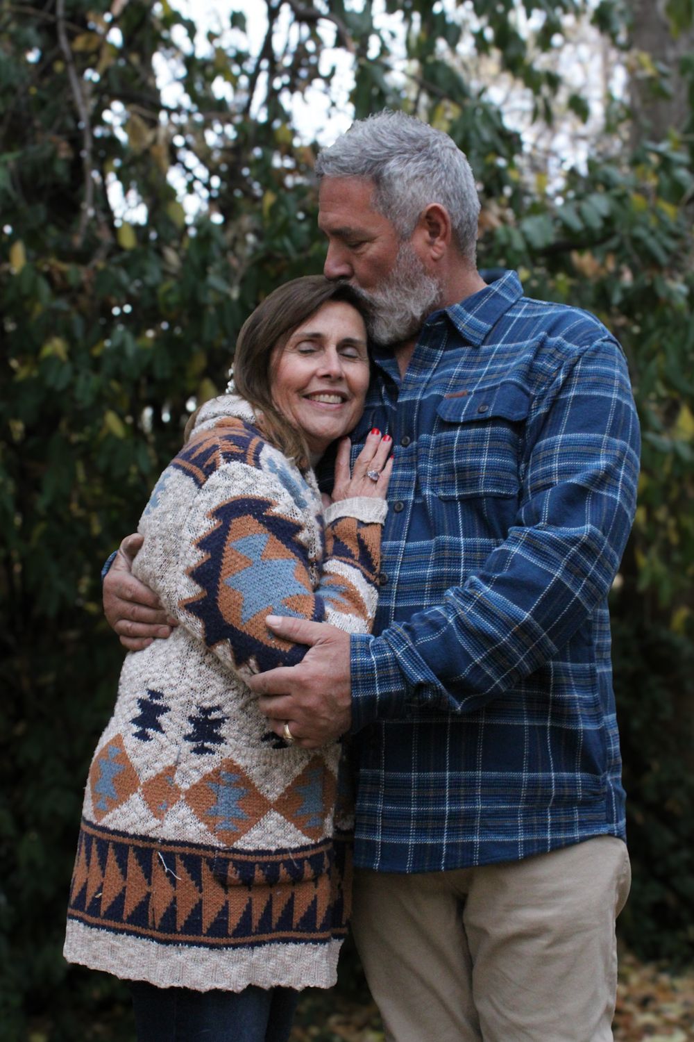 A couple embraces outdoors, wearing warm sweaters against an autumn backdrop.
