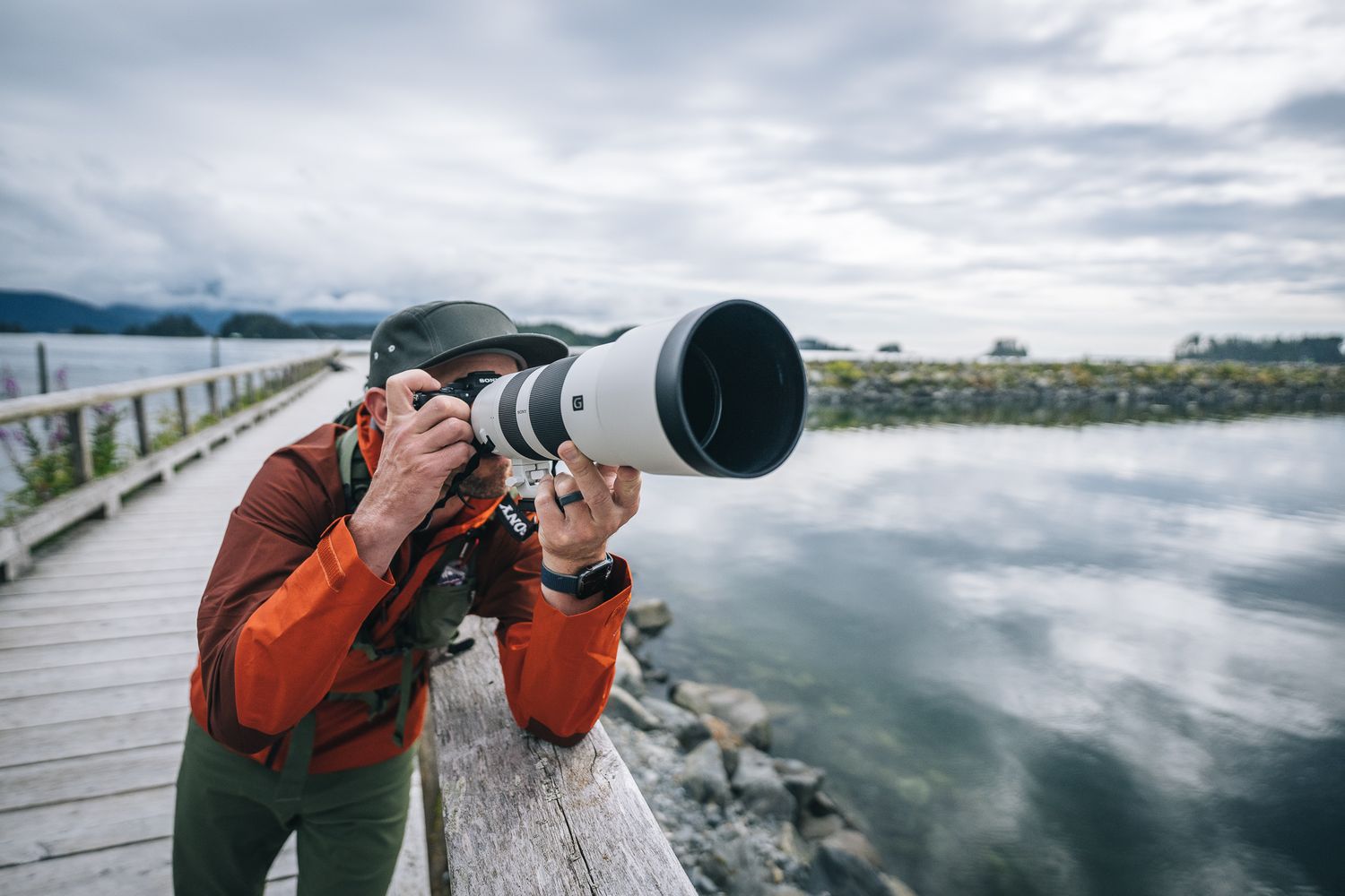 Photographer with large telephoto lens on wooden pier overlooking misty lake.
