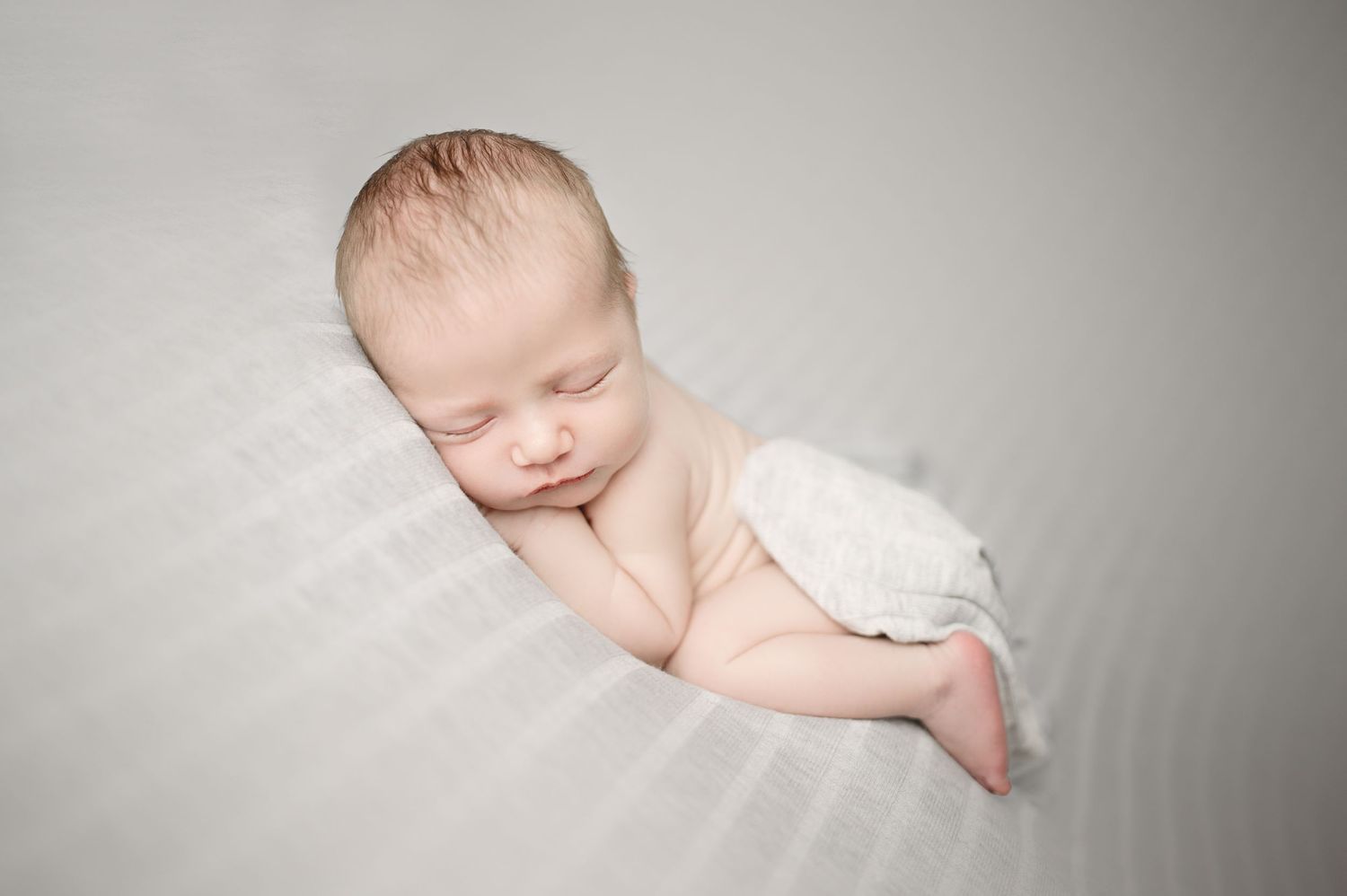 Professional newborn photography session with baby on grey backdrop.