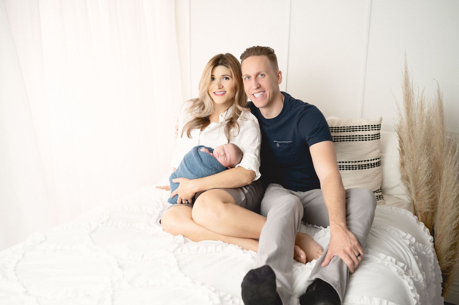 Family portrait with newborn baby in bright minimalist studio setting with pampas grass decor.