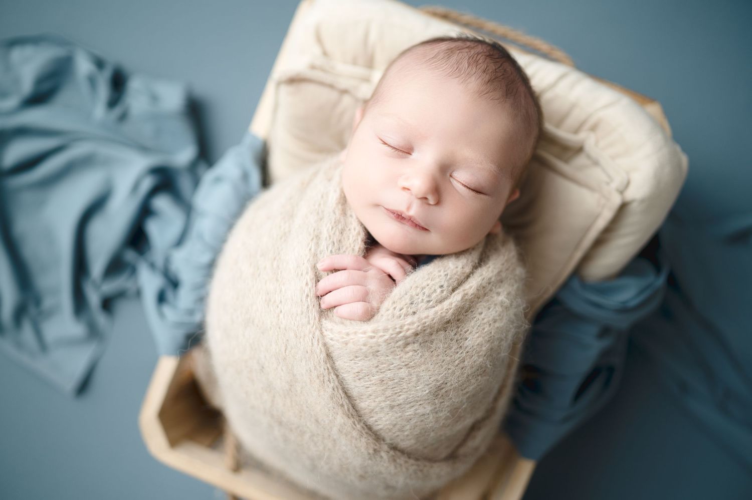 Artistic newborn portrait series with beige and blue tones against studio backdrop.