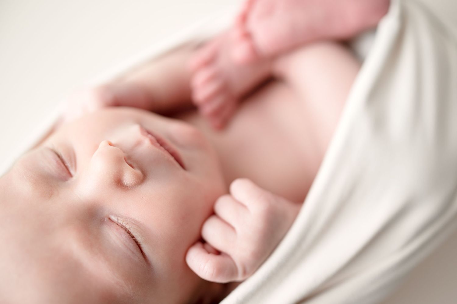 Peaceful sleeping newborn baby wrapped in white fabric.