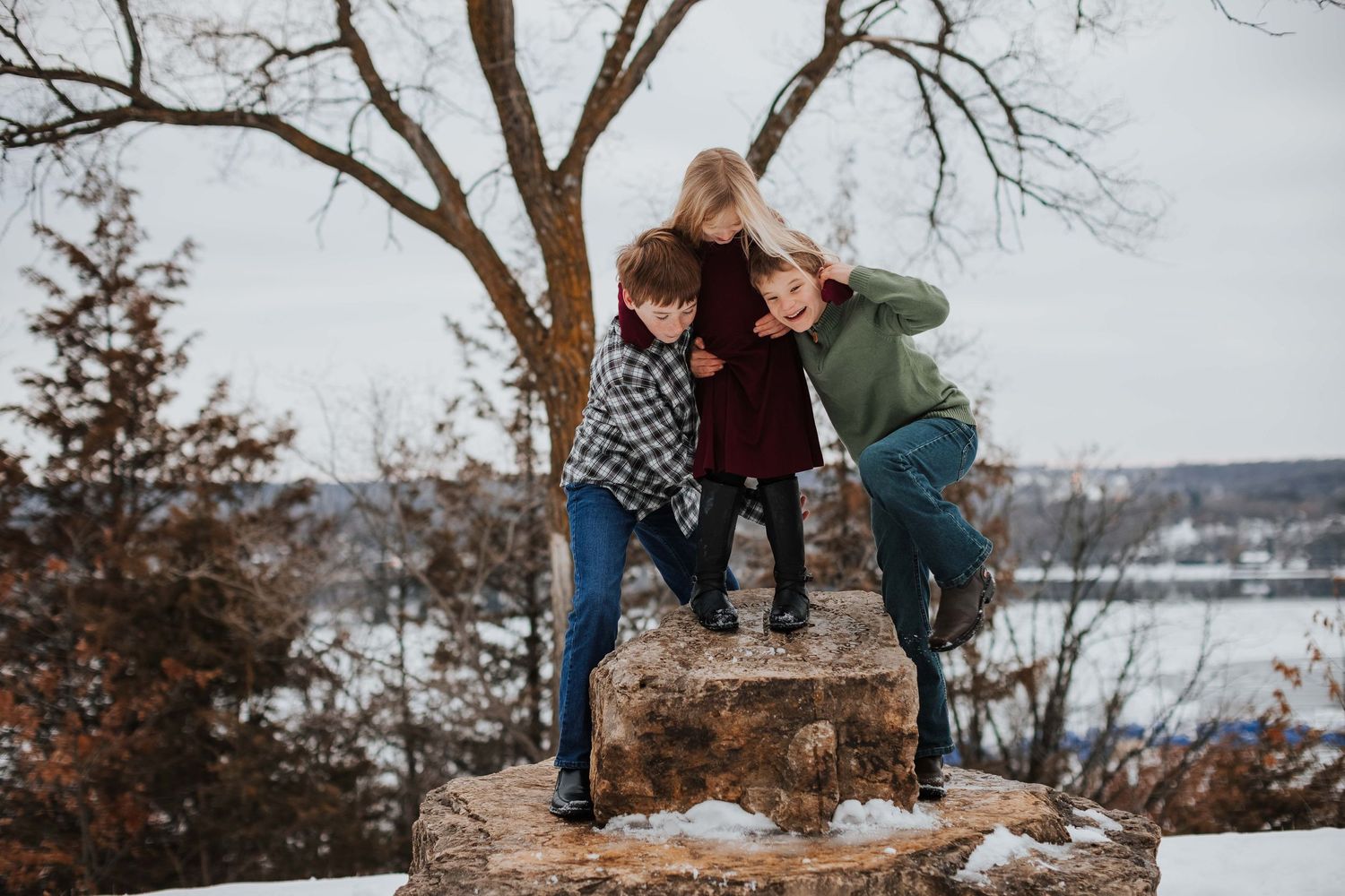 Three playful friends jump and pose together on a rocky overlook during autumn.