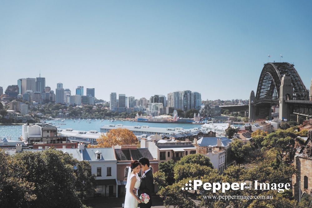 Wedding couple embracing with Sydney Harbour Bridge and city skyline in sunny background.