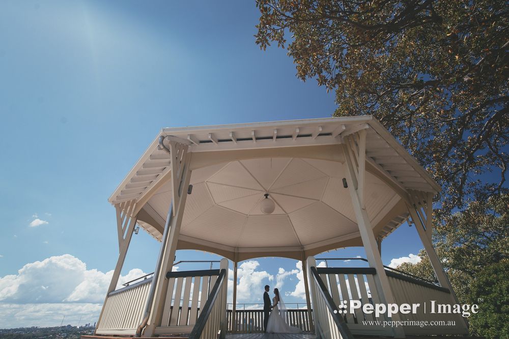 Wedding couple standing together under white gazebo pavilion against bright blue sky.