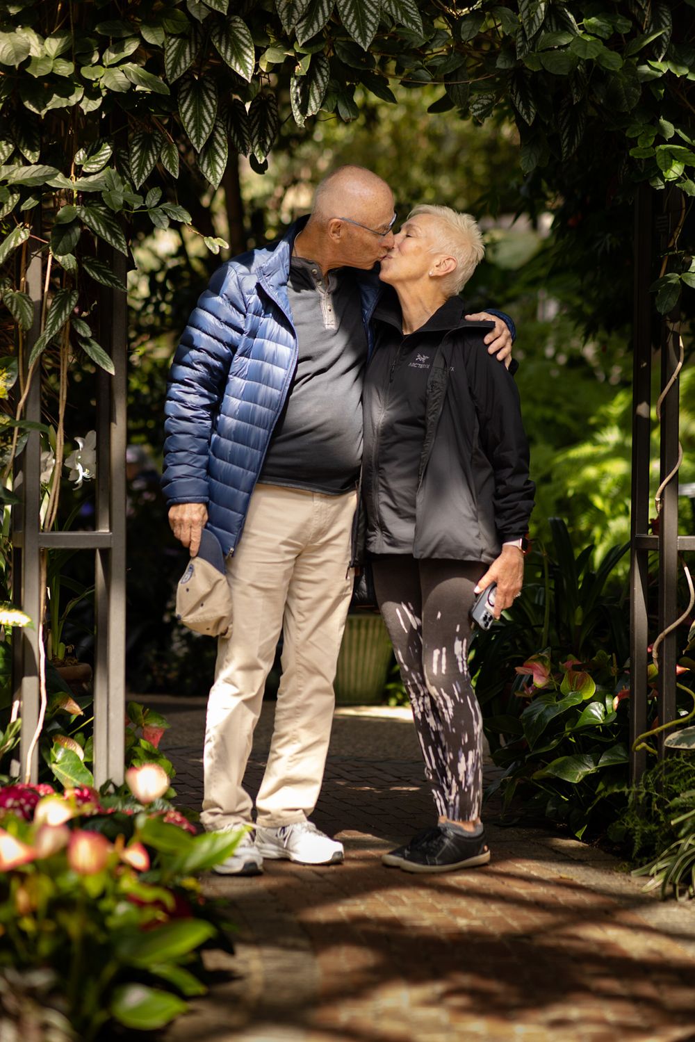 A couple shares a tender moment under a garden archway surrounded by greenery.