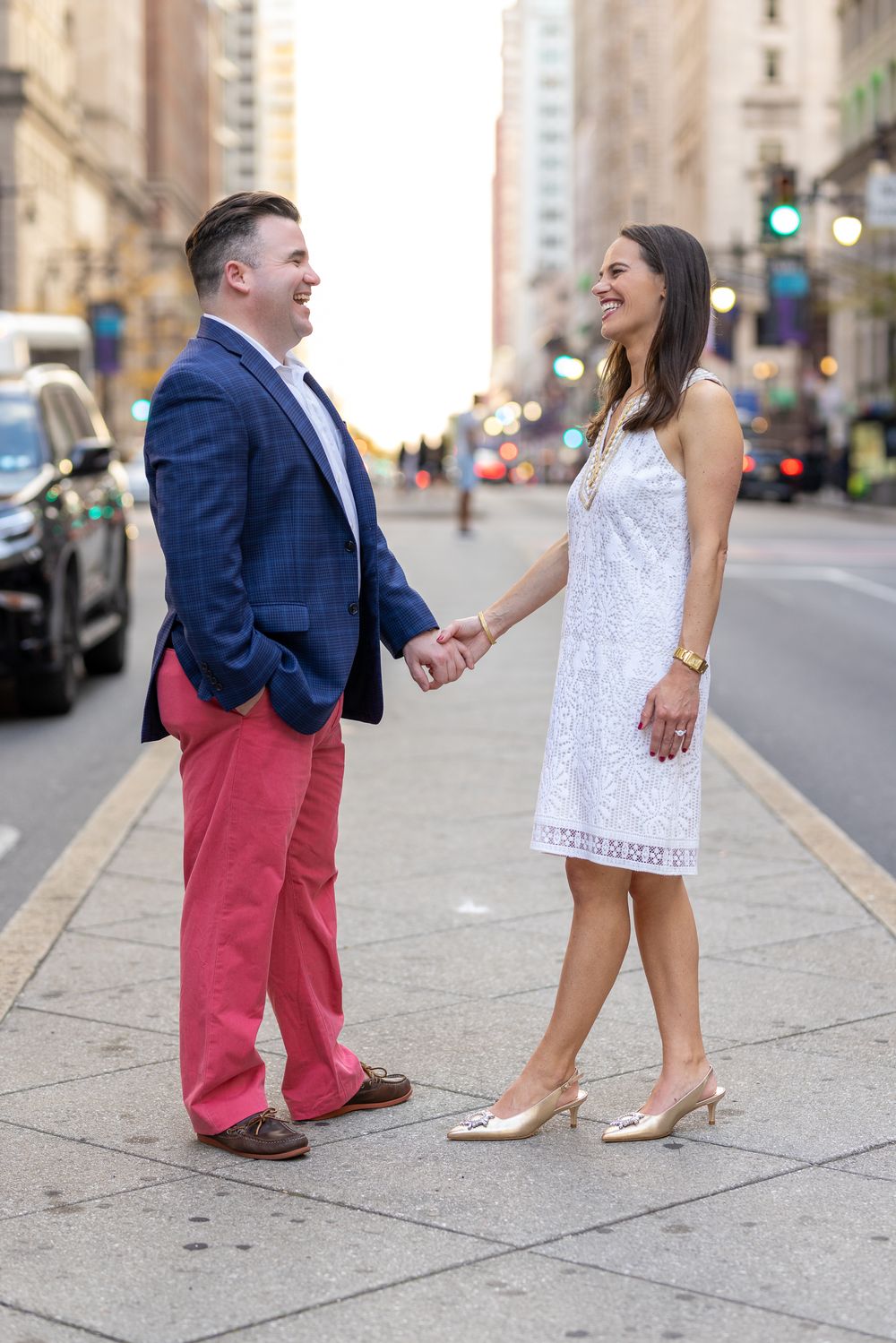 A couple shares a playful engagement photo session on a downtown city sidewalk.