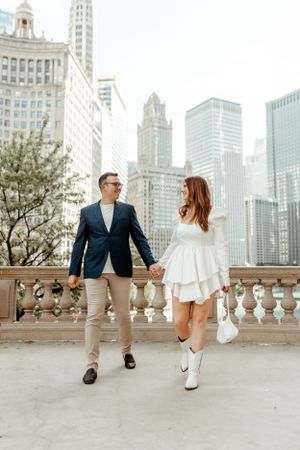 Elegant couple walking along stone balcony with Chicago skyline in background.