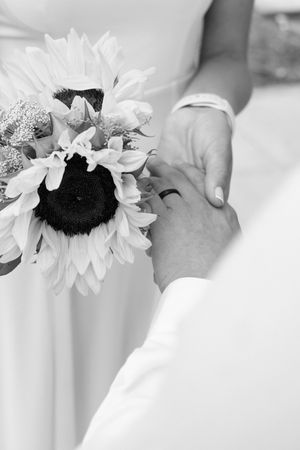 Black and white photo of hands holding sunflowers during an intimate wedding moment.