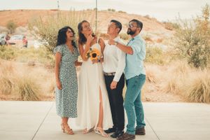 A joyful wedding party laughs together while posing in a desert setting.
