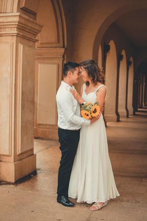 Romantic moment under archways with sunflower bouquet and flowing white dress.