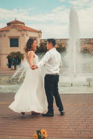 Dancing by a fountain in formal attire with Spanish colonial architecture in background.