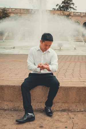 Person in white shirt sitting on brick ledge near fountain in romantic outdoor setting.