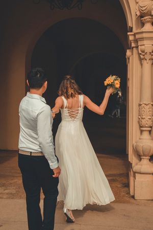 Couple walking through archway with bride holding sunflowers in flowing white dress.