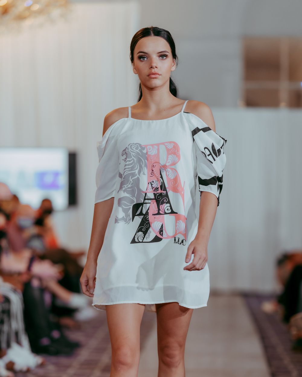 Fashion model showcases white graphic top and minimalist styling on catwalk.