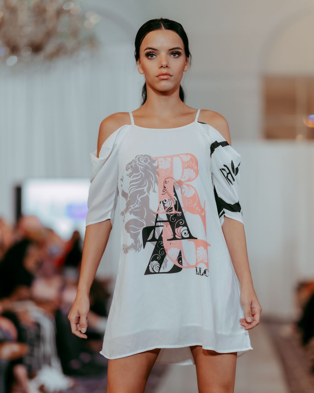 Model demonstrates flowing white top with artistic print during fashion presentation.