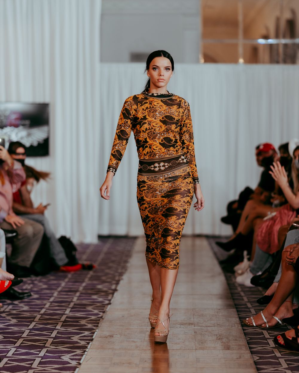 Designer dress with baroque orange and black print showcased on fashion show catwalk.