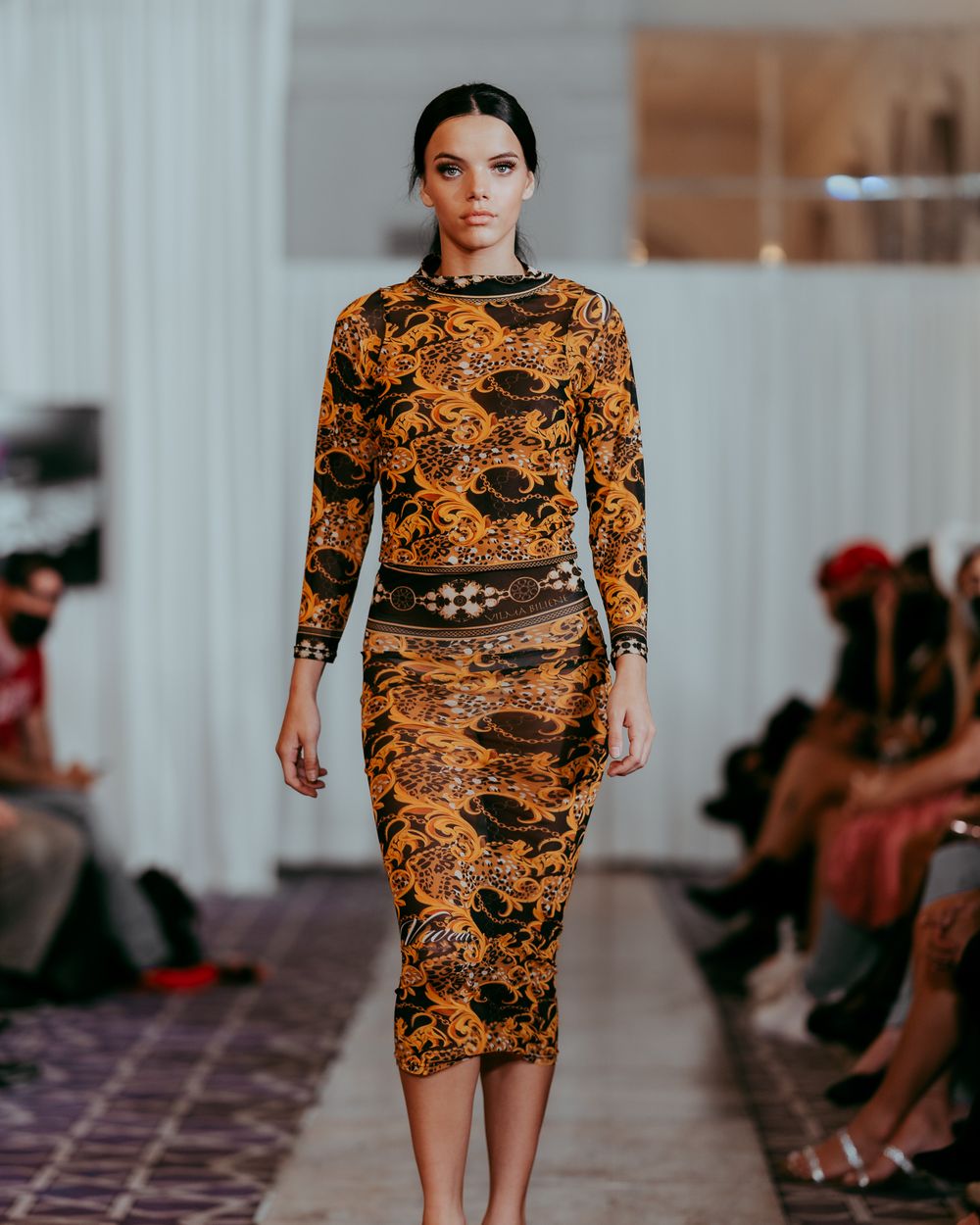 High-end fashion show featuring fitted dress with striking orange and black baroque design.