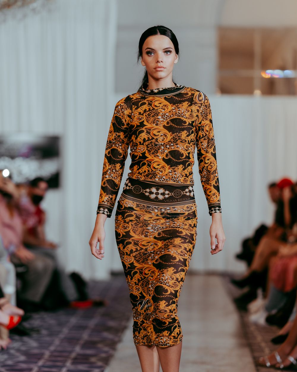 Runway model showcasing elegant orange patterned dress with dark trim detail.
