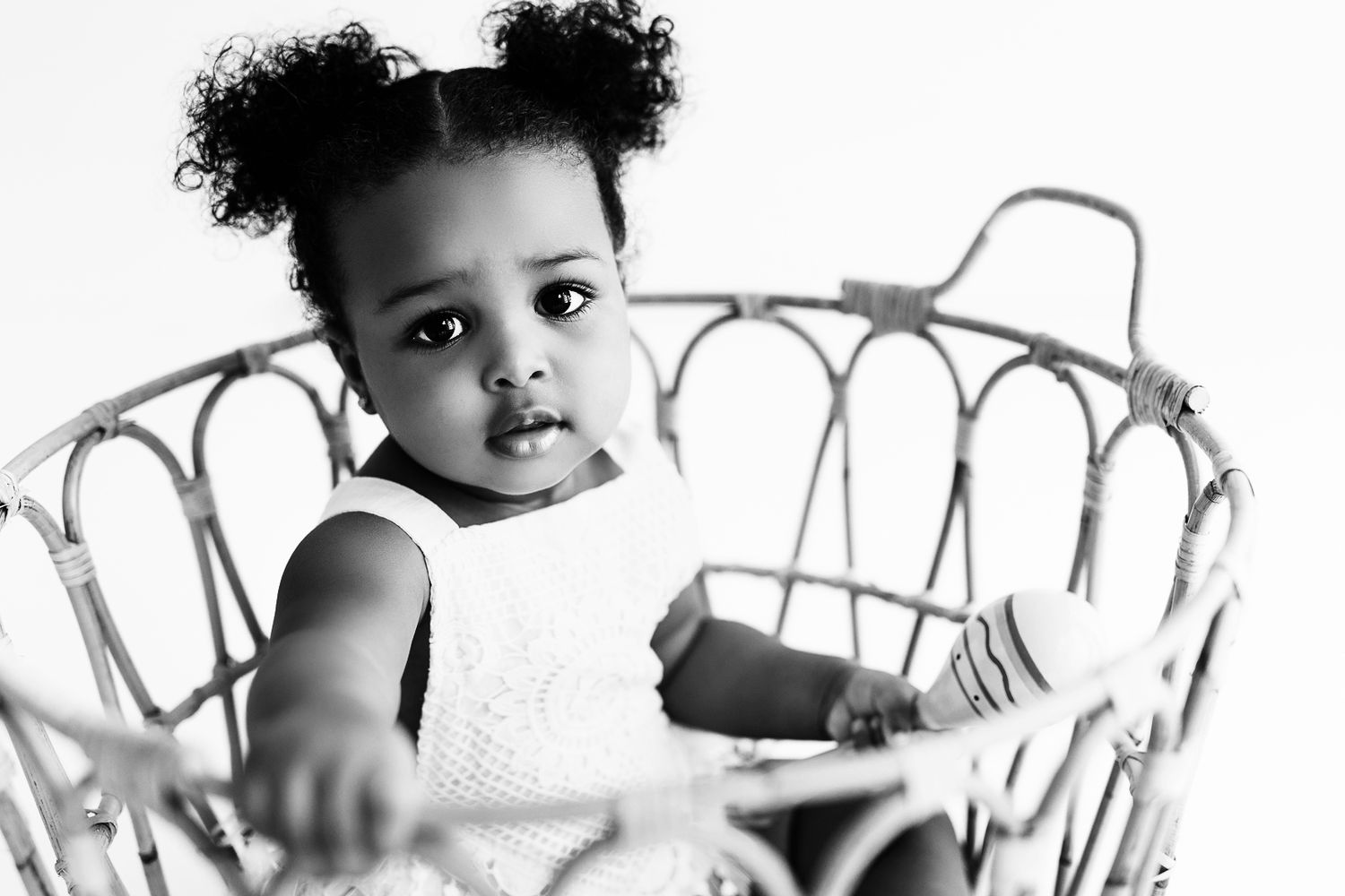 Black and white portrait of a young child sitting in a vintage wire basket.