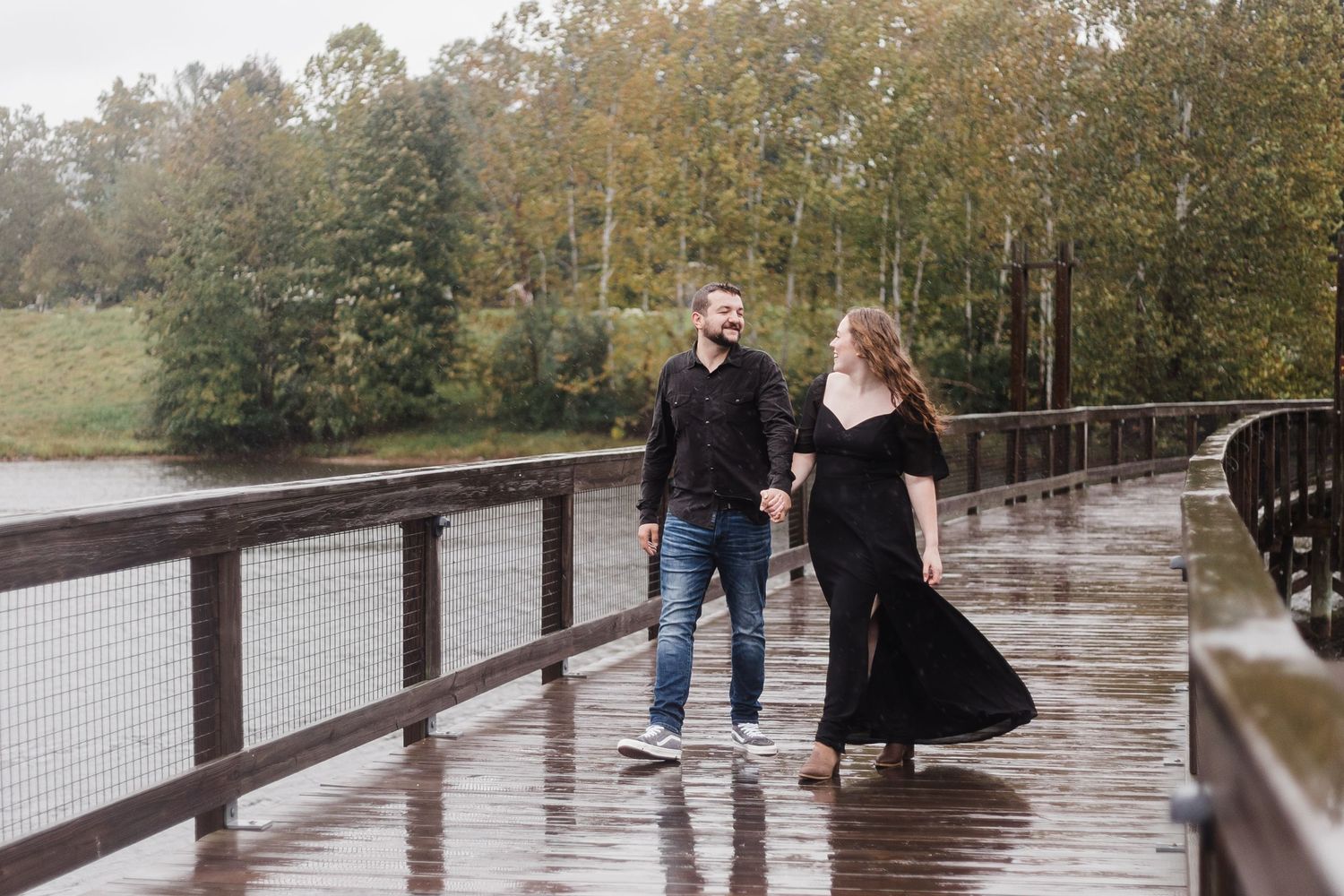 Couple shares tender moment on rain-soaked wooden deck with lake view in background.