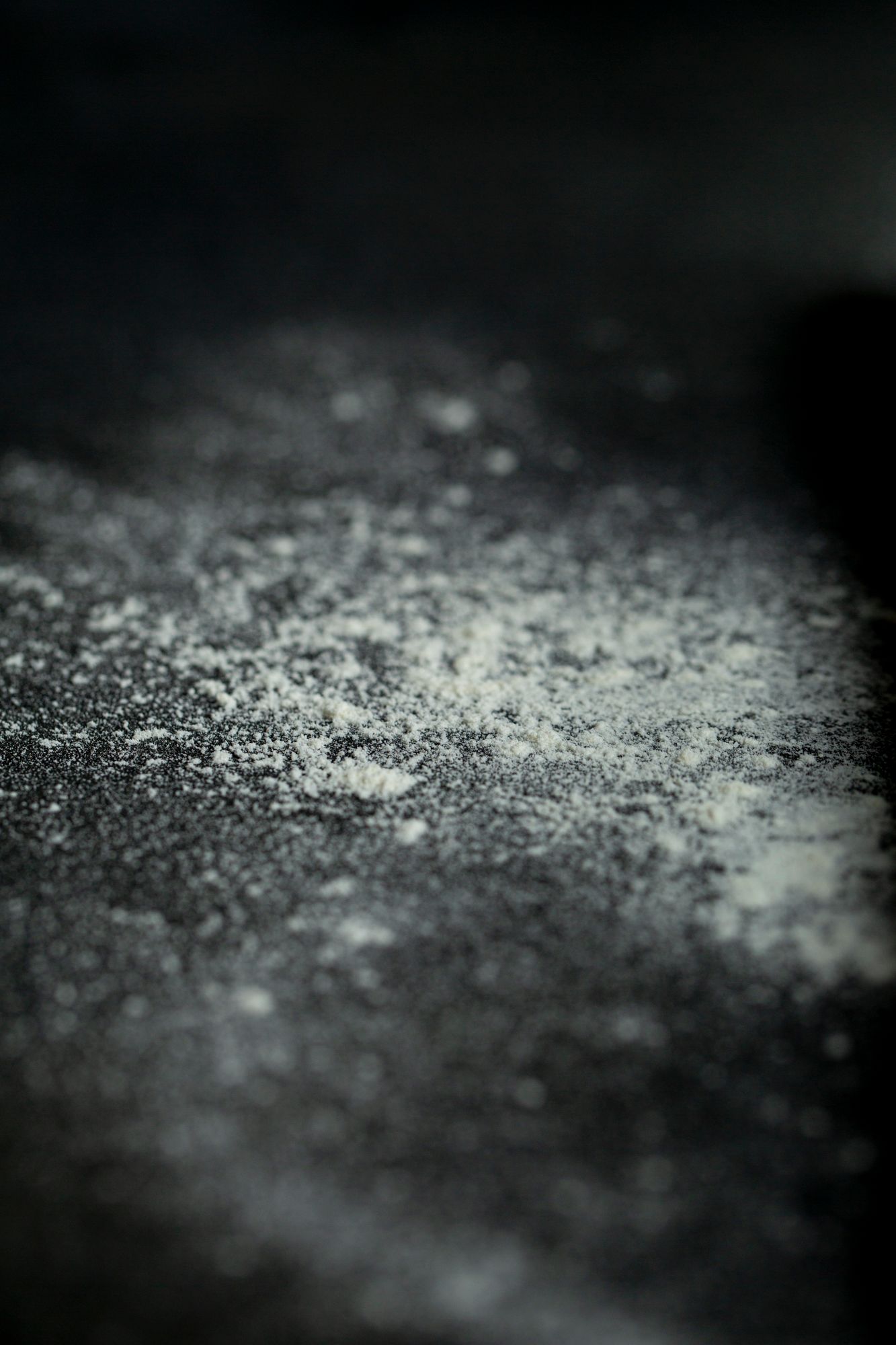 Dark moody background with scattered flour dusting creating atmospheric texture.