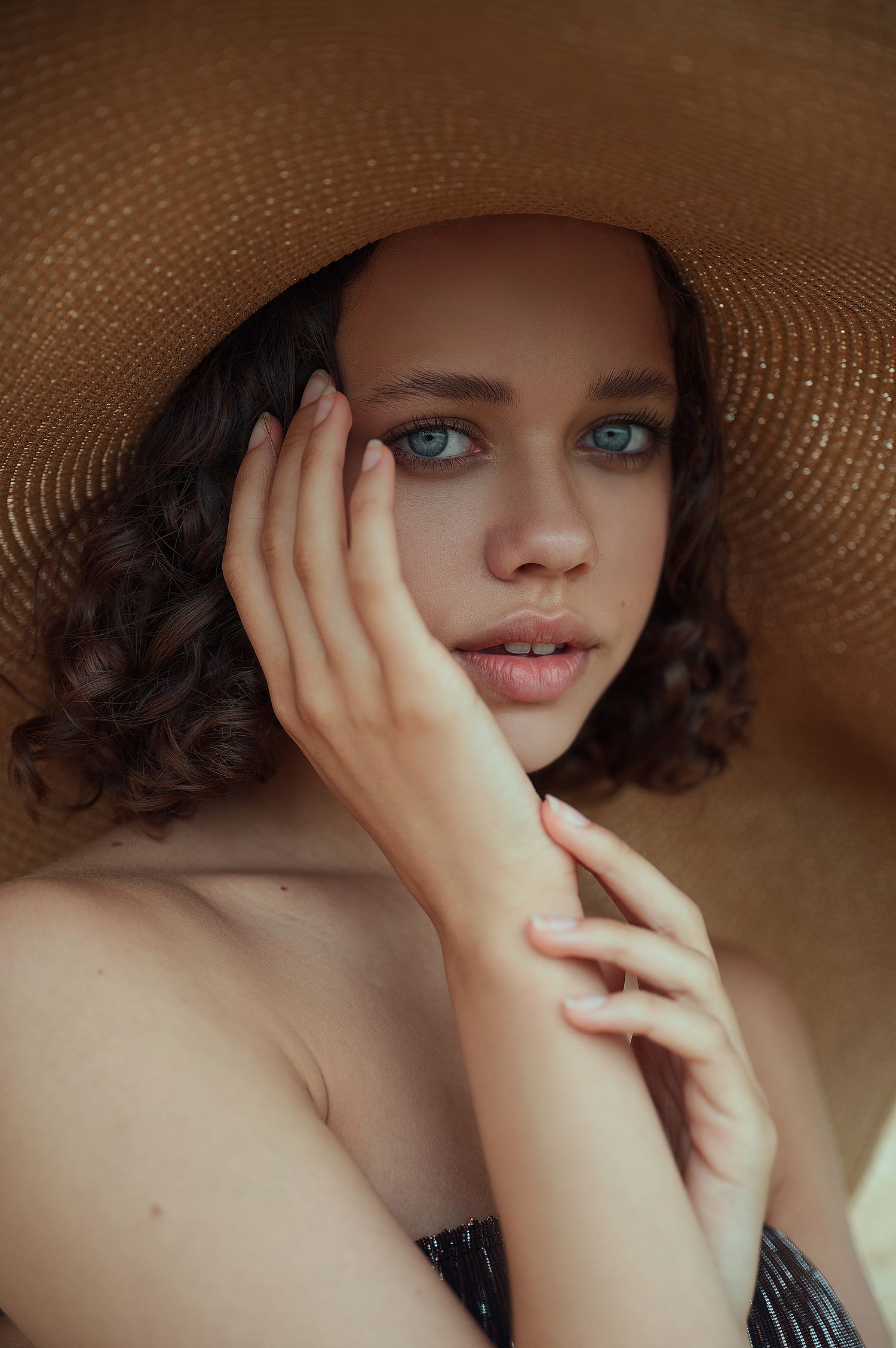 Close-up beauty shot under straw hat shows striking blue eyes and natural makeup.