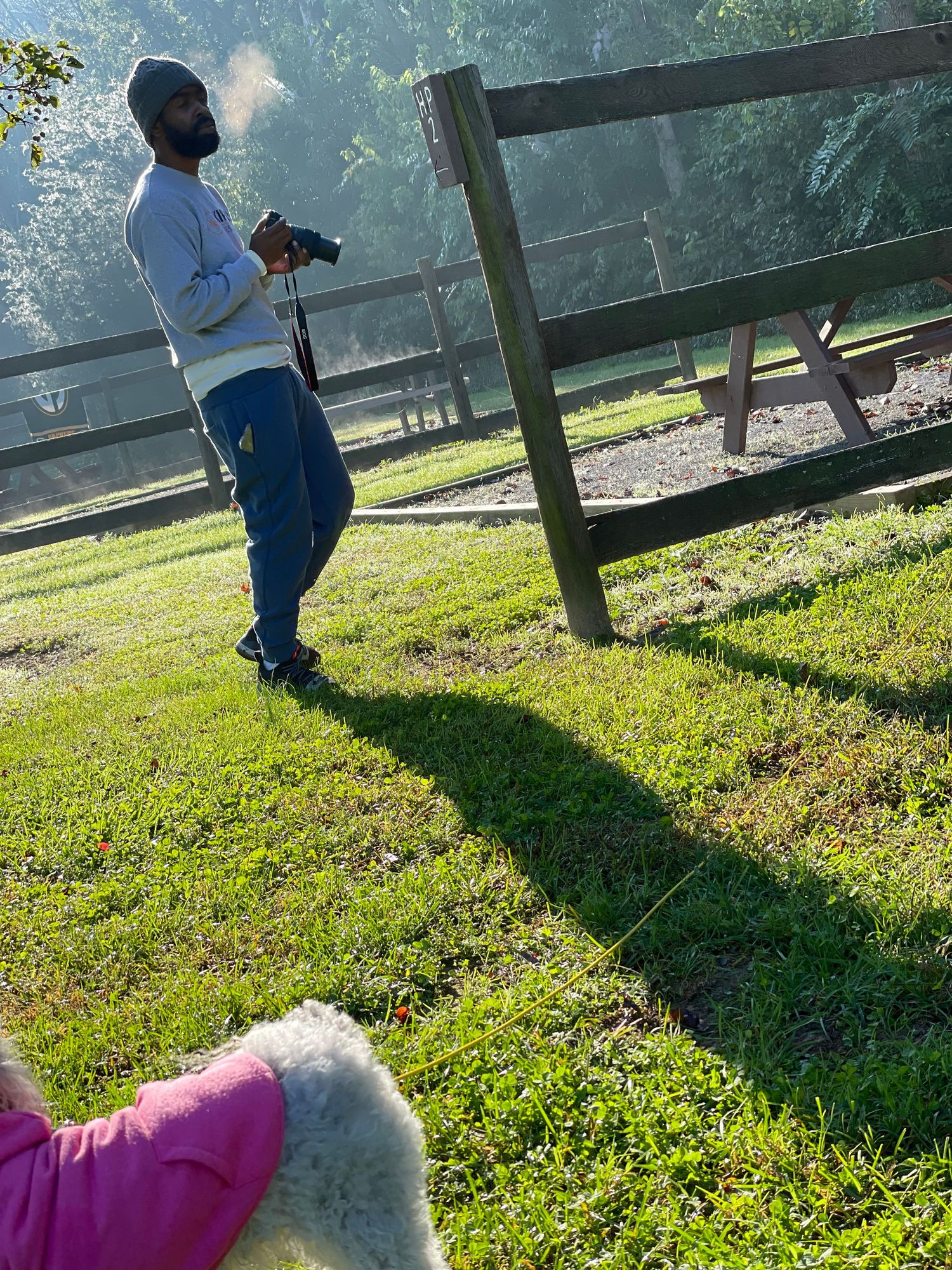 Person smoking outdoors near a wooden fence in a grassy area.