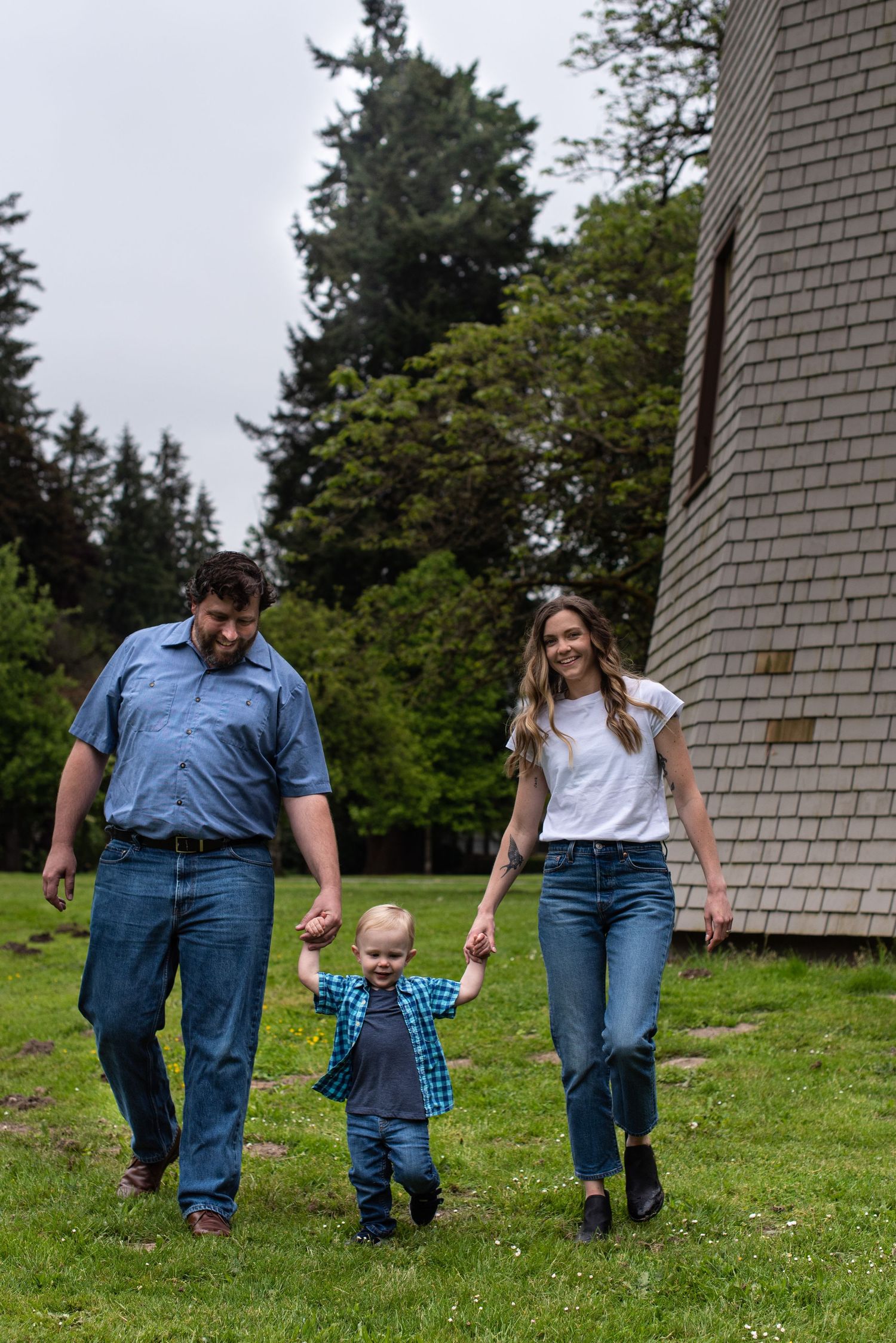 Young couple with baby walking by a windmill for a photo session at Marymore Park in Redmond, WA.