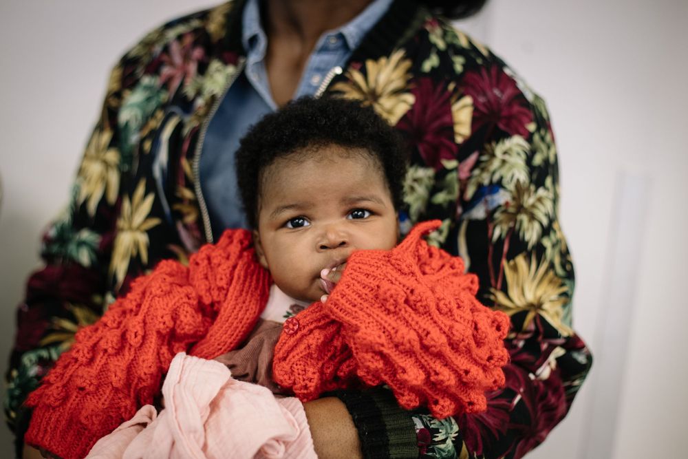 Baby wrapped in bright red knit blanket against floral print background.