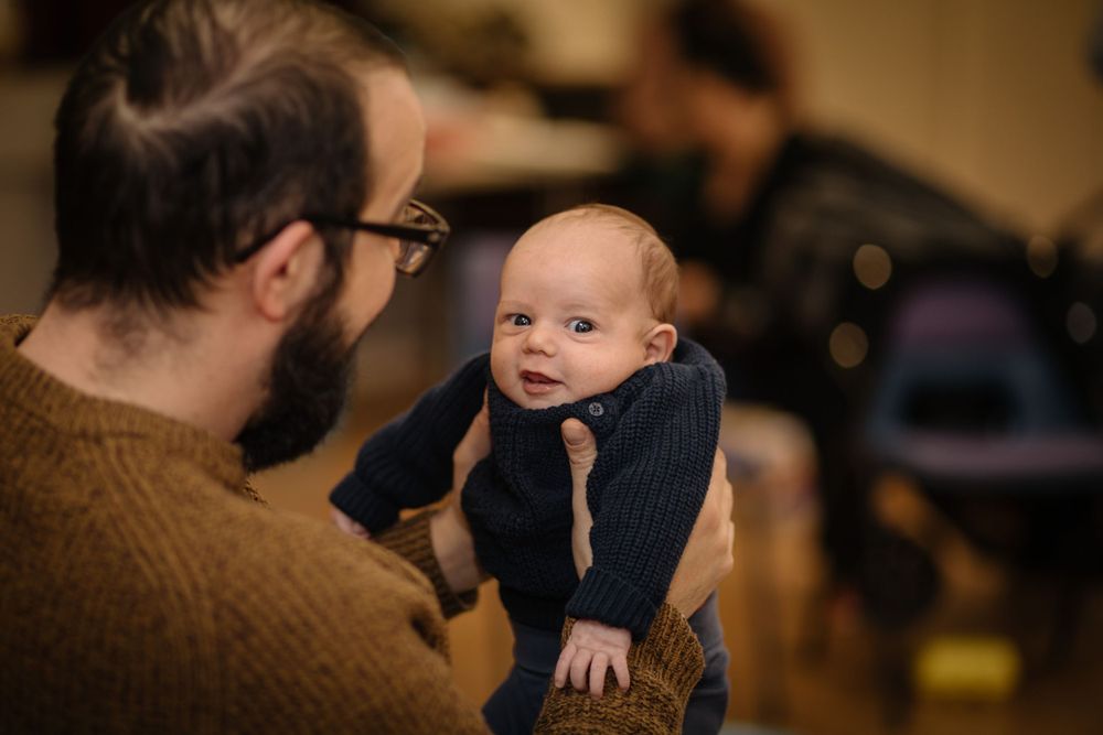 Baby in navy outfit shares special moment with parent wearing brown sweater.
