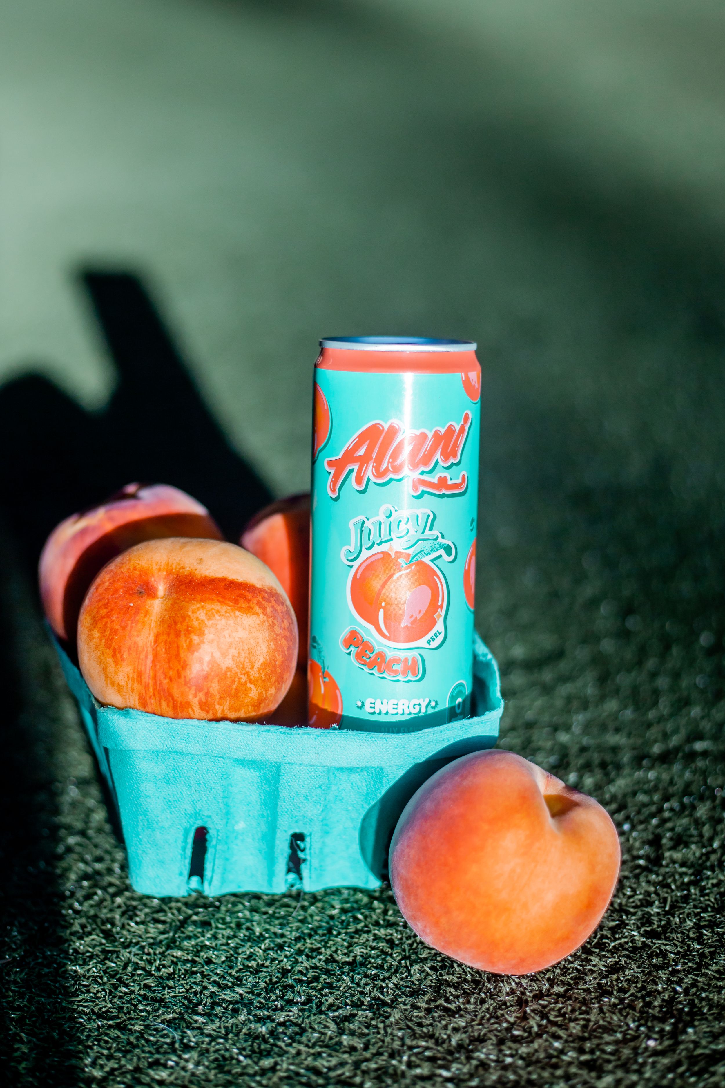 Alani beverage can with fresh peaches on a turquoise basket against dark background.