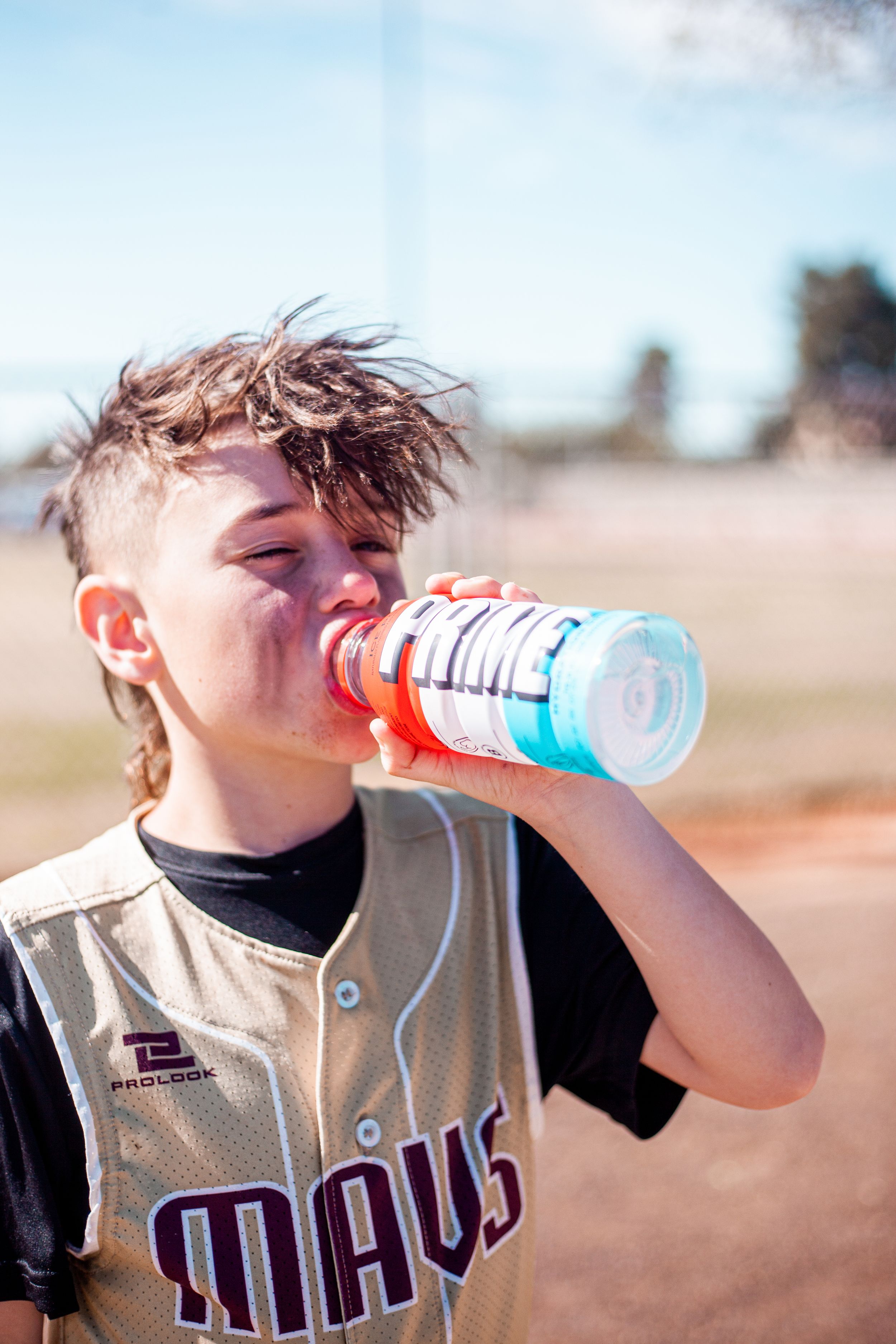 Young baseball player in uniform drinking from a sports beverage bottle outdoors.