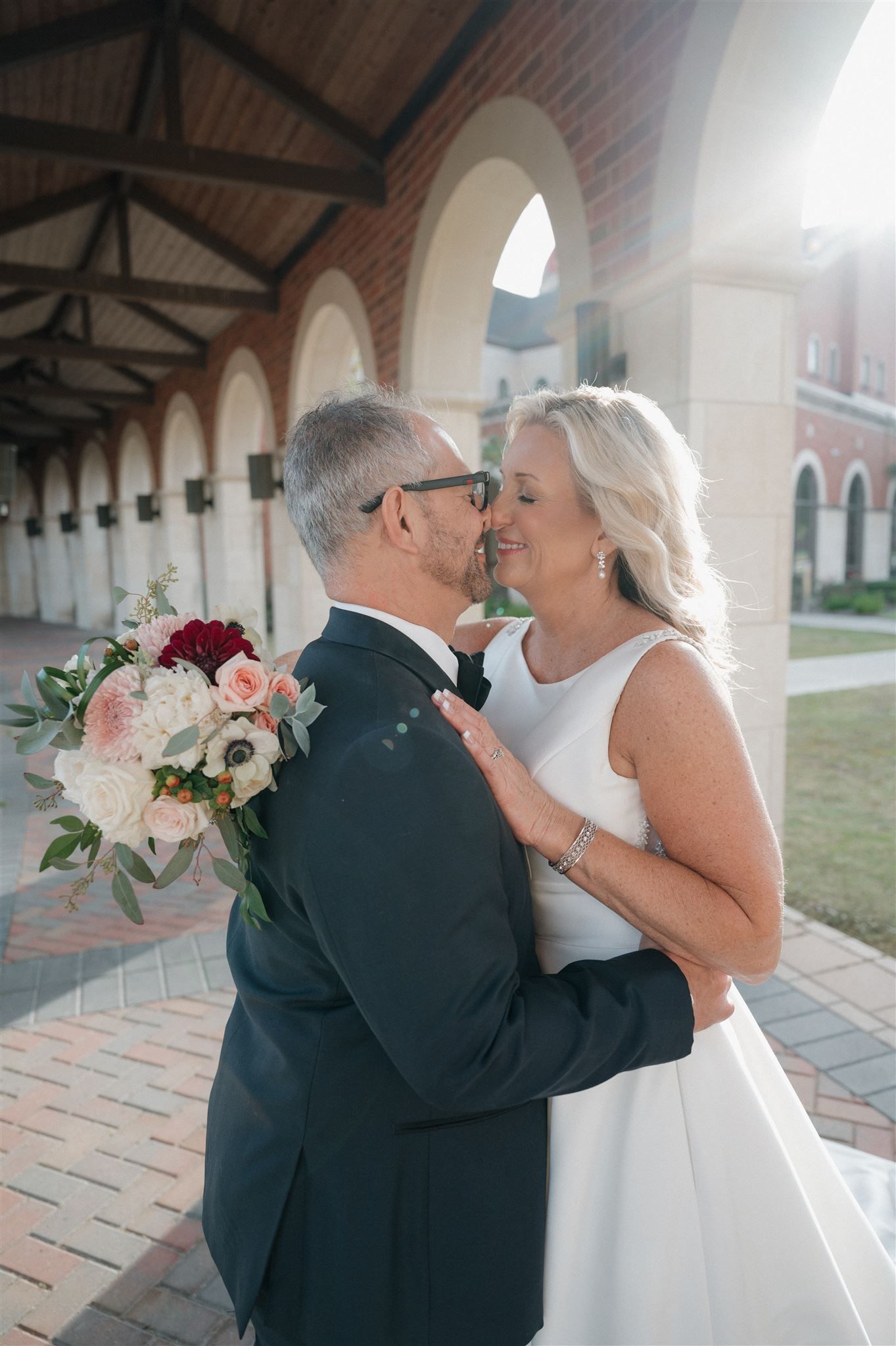 Romantic moment between couple with bouquet under arched colonnade.