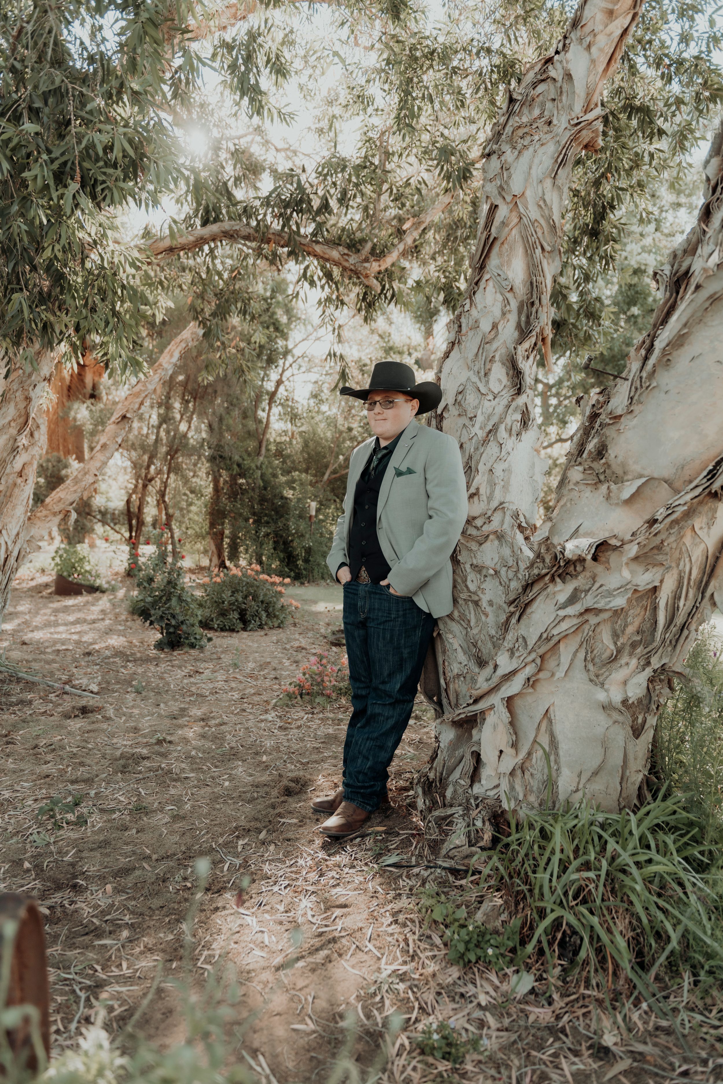 A person in western attire poses against a backdrop of eucalyptus trees.