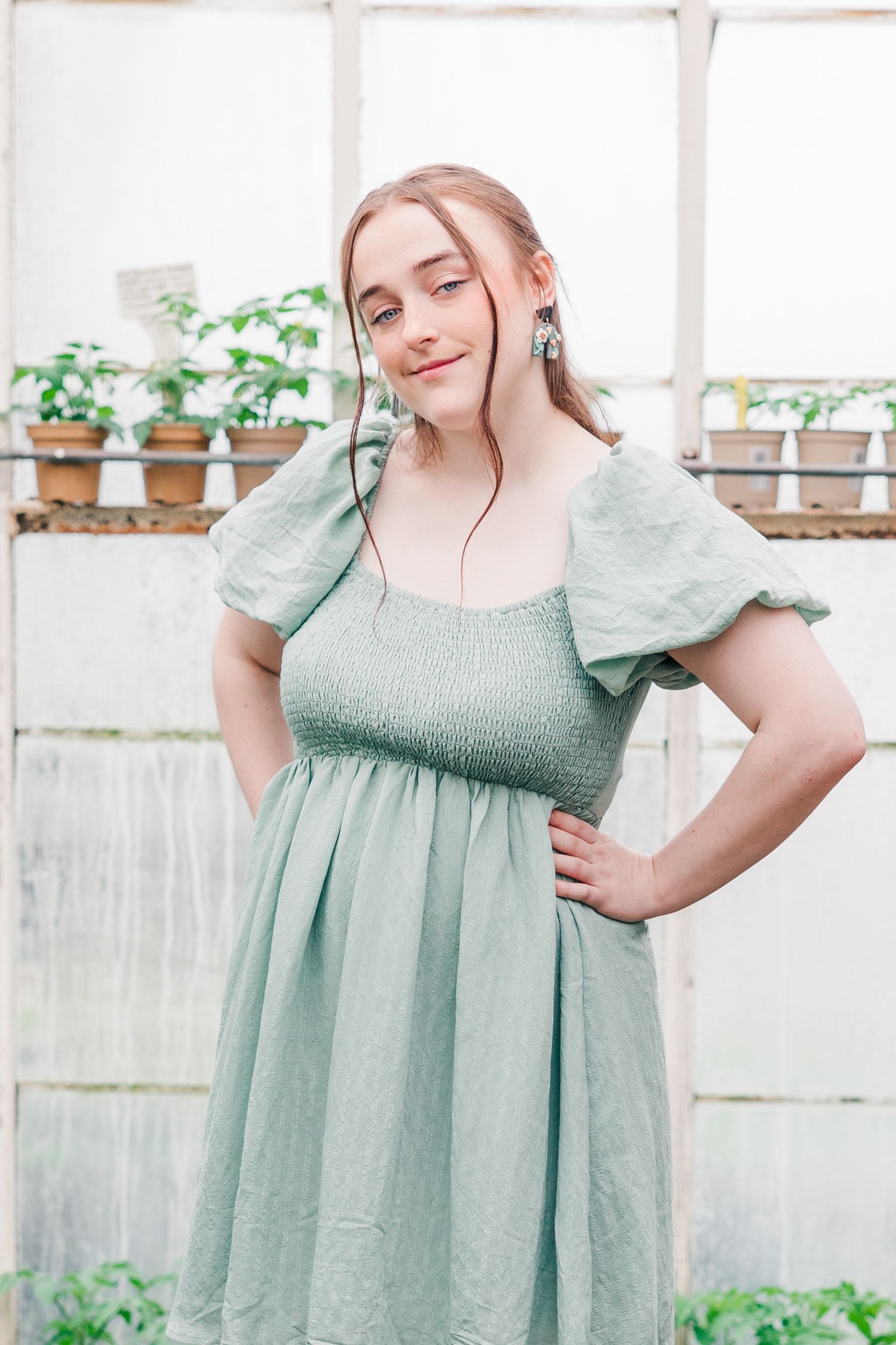 Portrait shot in greenhouse wearing sage green dress with puff sleeves.