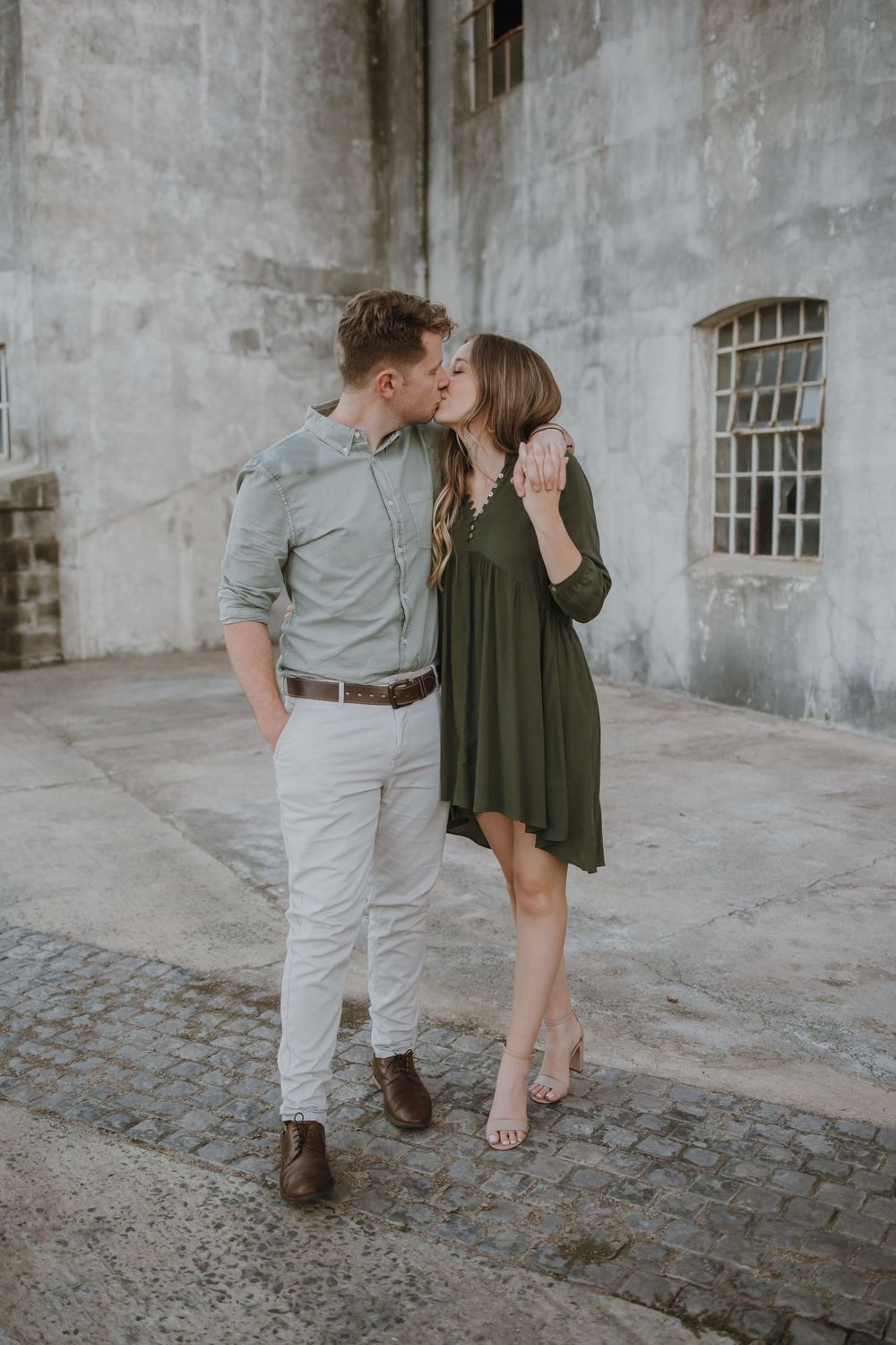 A romantic couple sharing an intimate moment against an industrial concrete wall.