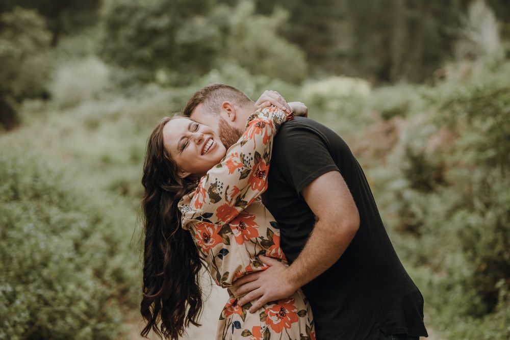 A couple shares a joyful embrace in a lush green forest setting.
