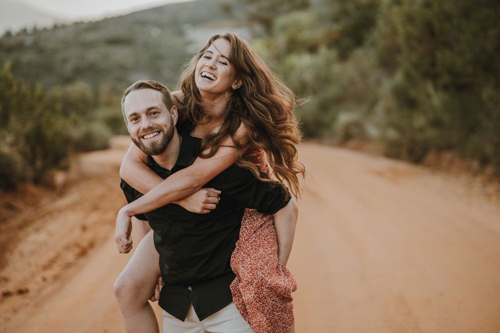 Playful piggyback ride on dirt trail during sunset engagement session.