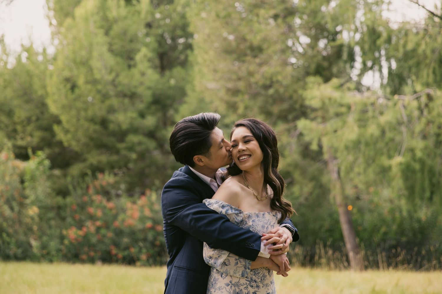 Joyful couple embracing and laughing together in a sunny outdoor garden setting.