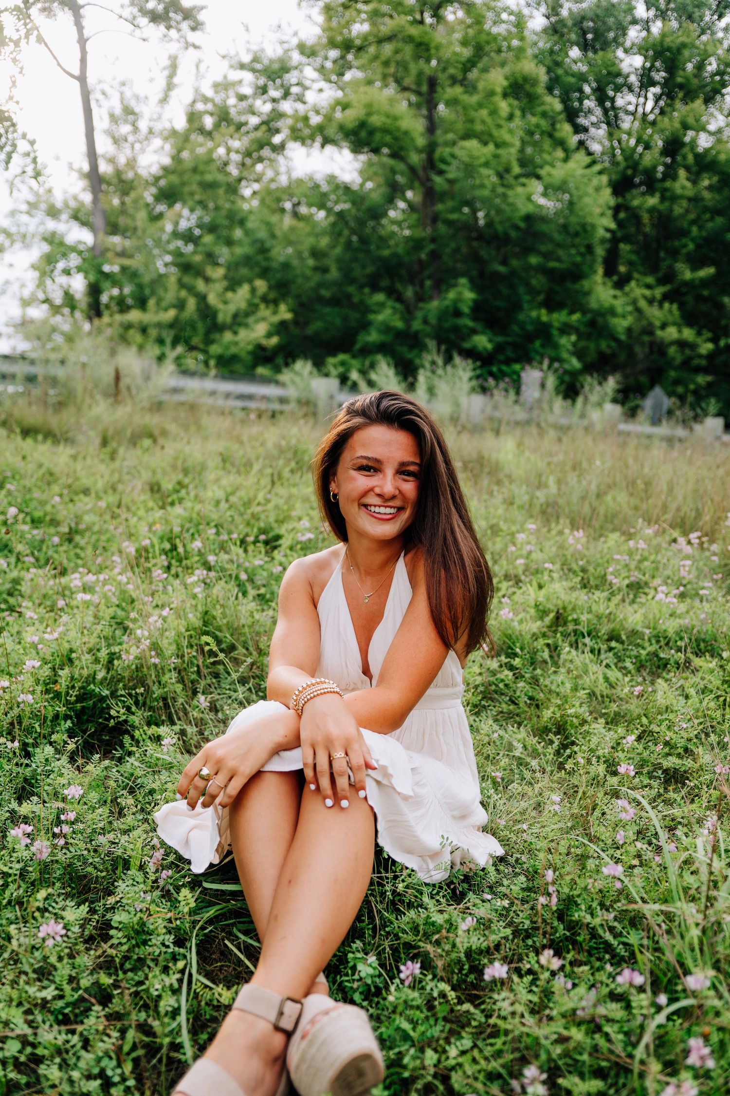 Person in white dress sitting joyfully in blooming wildflower field.