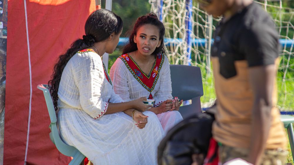 People sitting at an outdoor festival event with colorful decorations and tents.