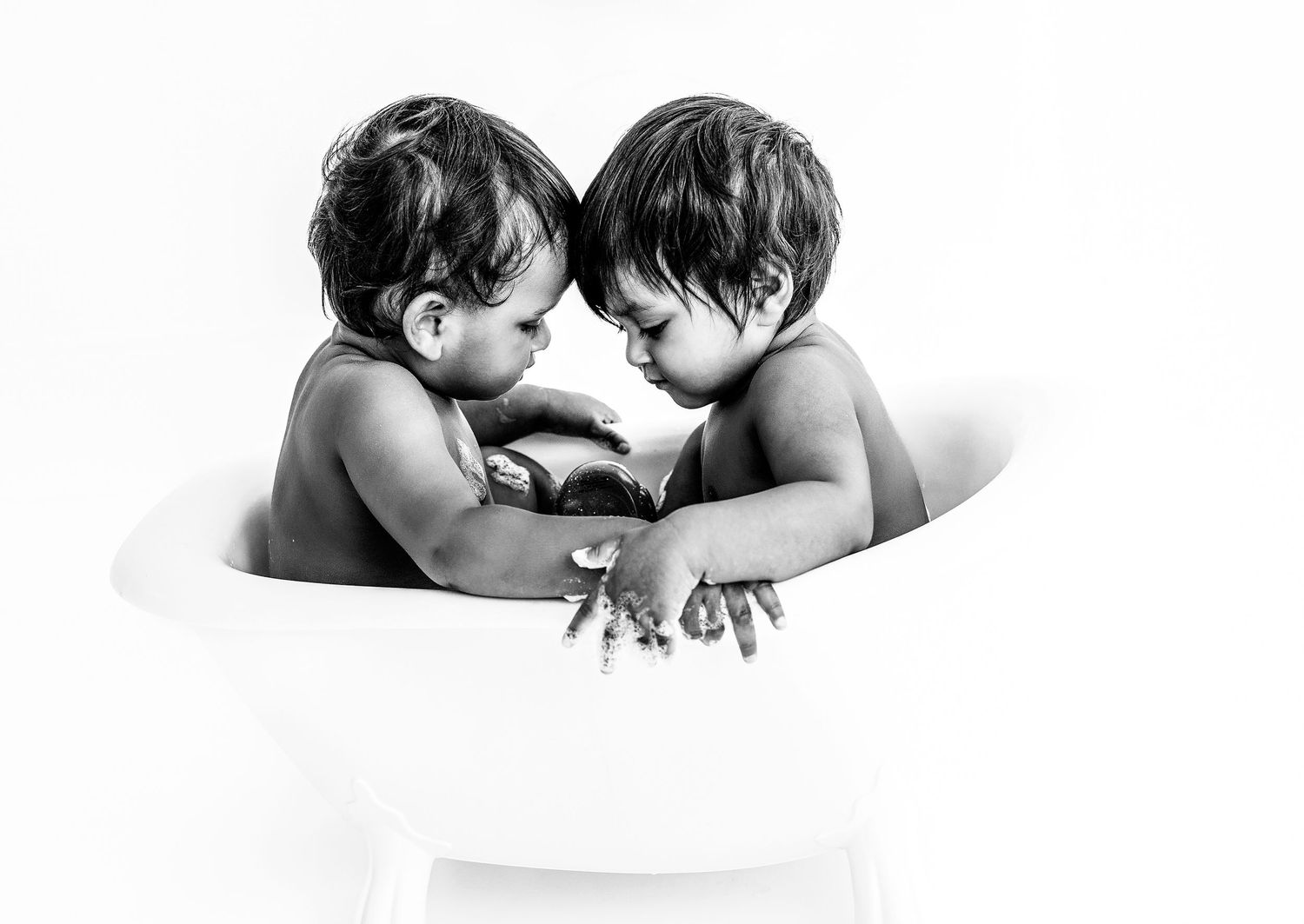 Two young siblings share an intimate moment while sitting in a white bathtub.