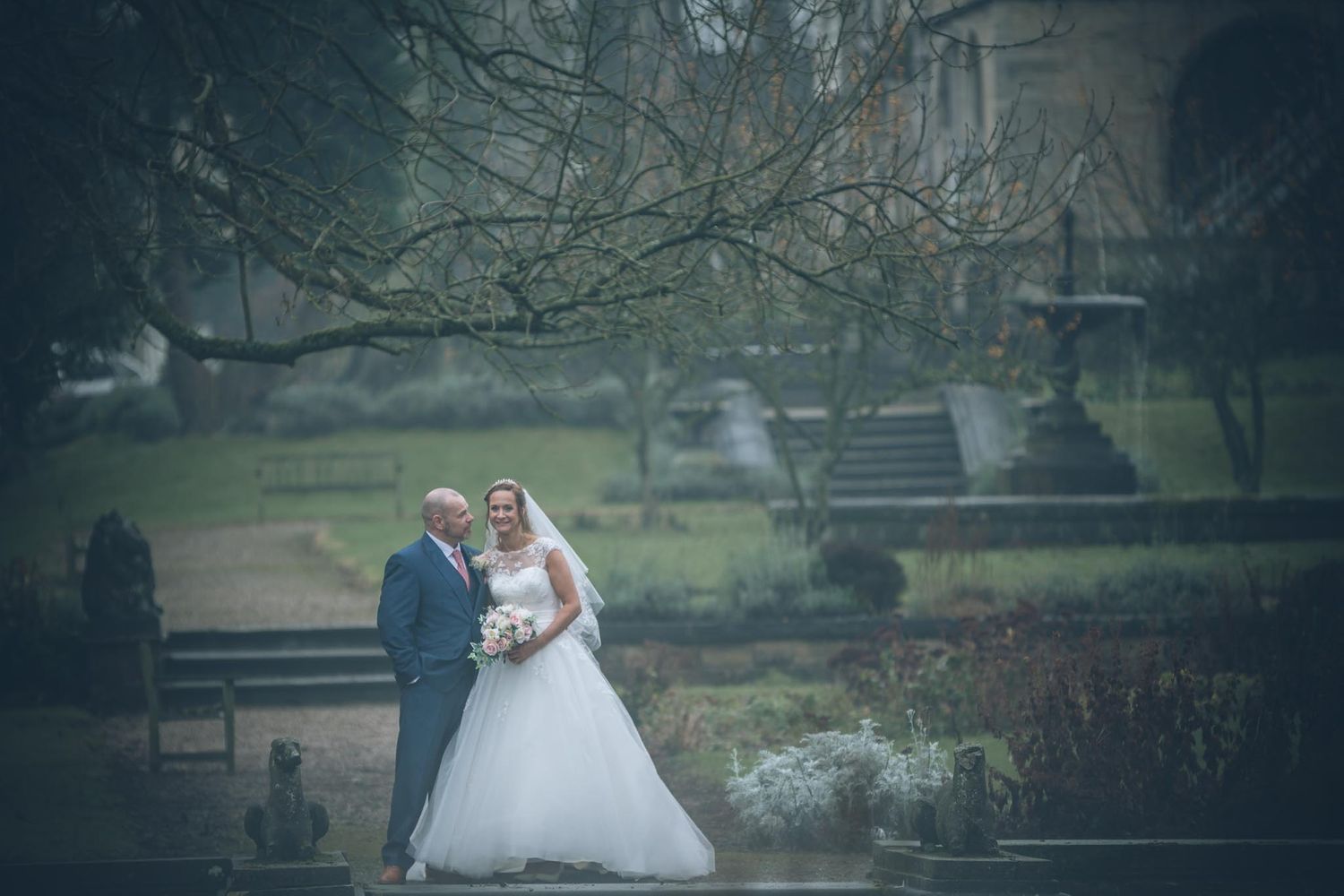 Wedding couple poses for romantic portrait in misty garden setting.