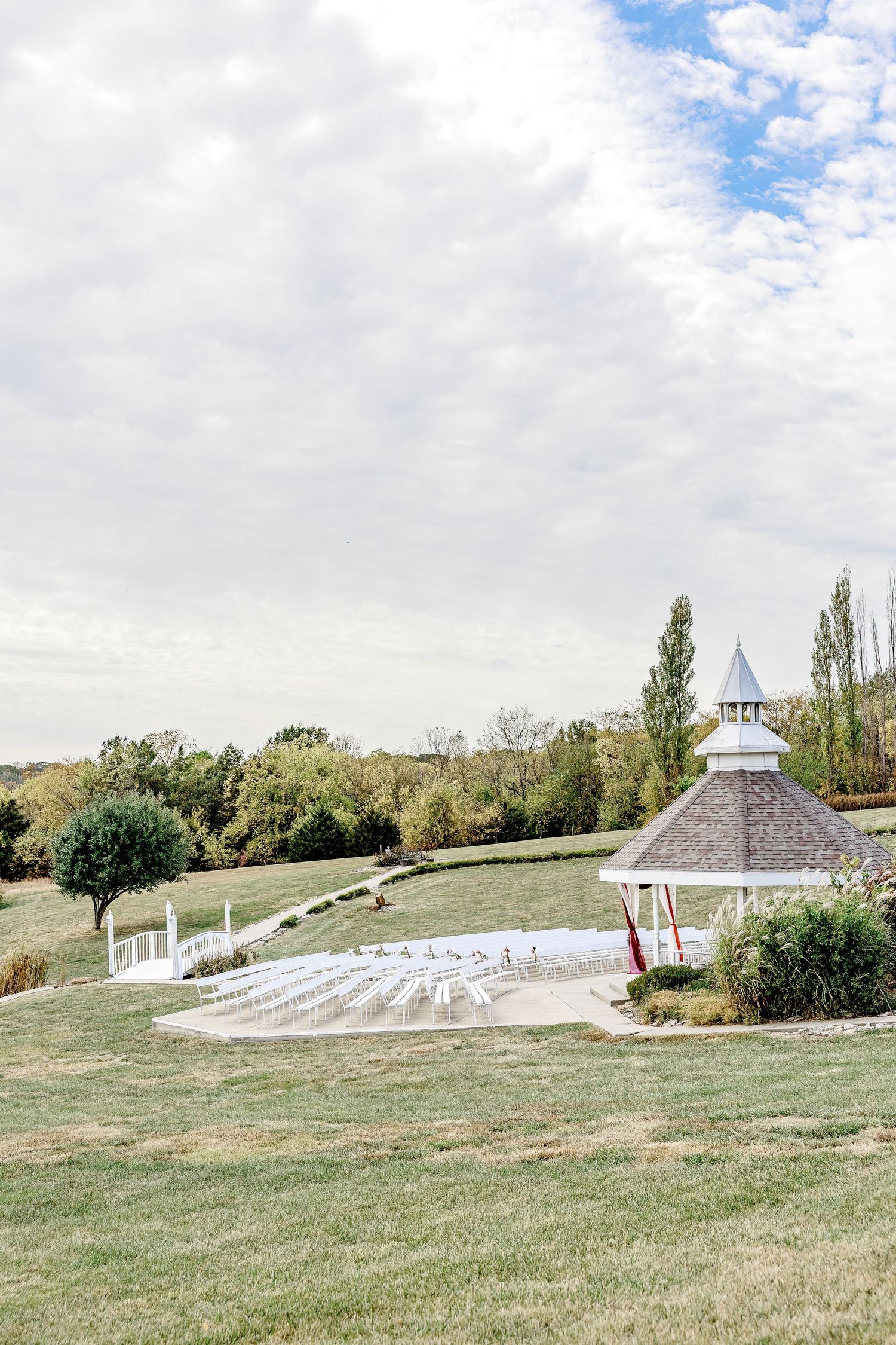 White gazebo and chairs set up for an outdoor wedding ceremony on a scenic hillside under cloudy skies by Stephanie Coulter Photography