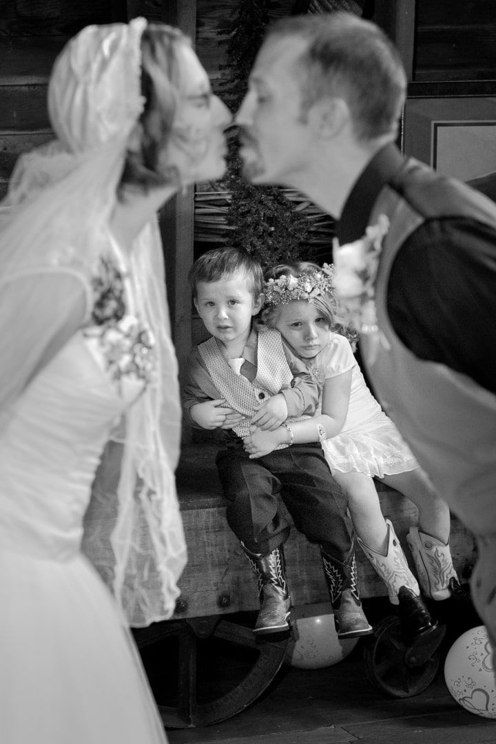 black and white of bride and groom kissing with children looking terrified in background during wedding in Graham, WA