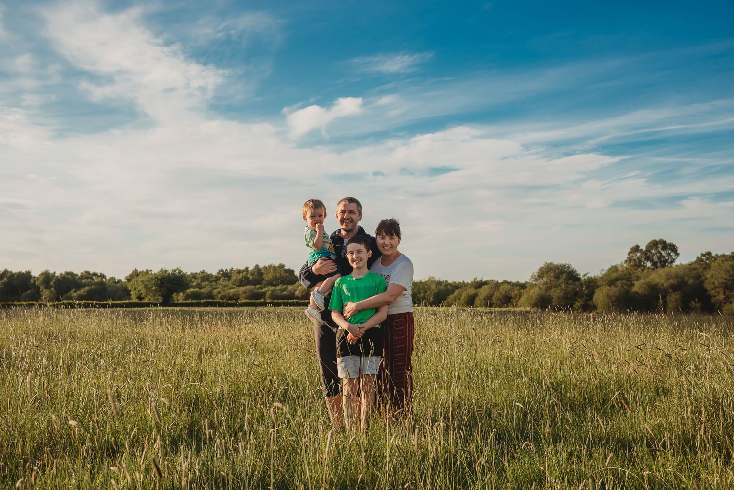 You & Me Photography's Shauna, with her family for a photo, taken in a field with long grass.