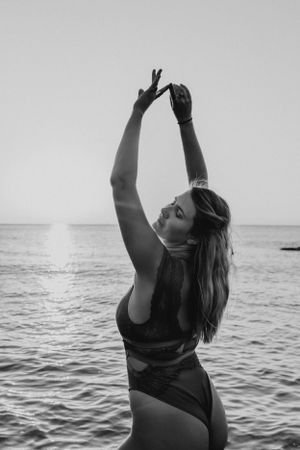 Silhouette of person in swimwear posing with raised arms against ocean backdrop in black and white.