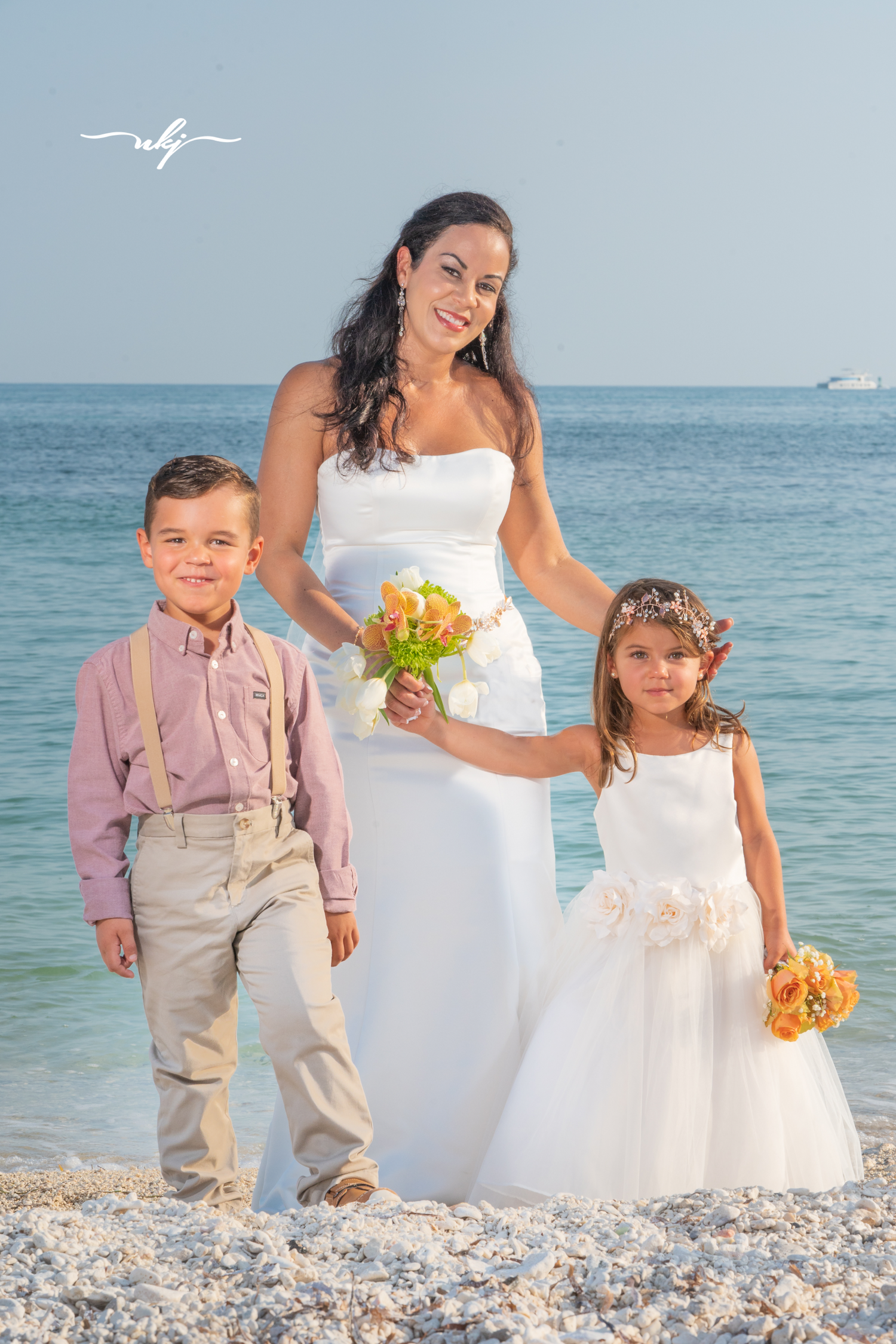 Beach wedding photography featuring a bride and children on white sand.