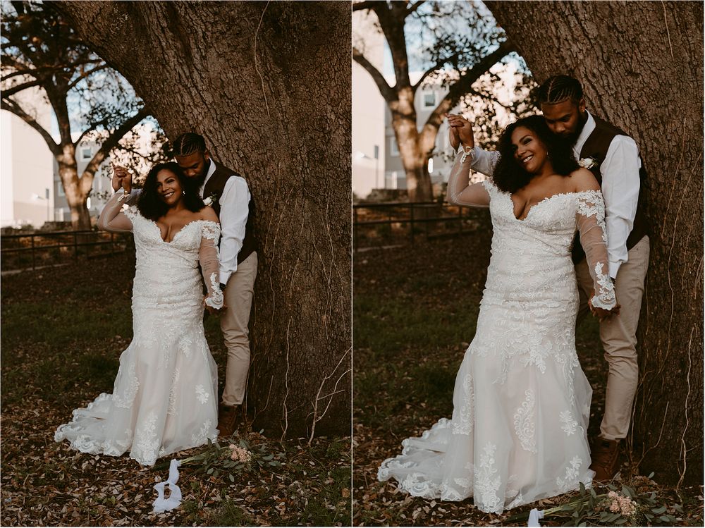 Romantic wedding couple embraces against a large tree trunk during sunset golden hour photography session.